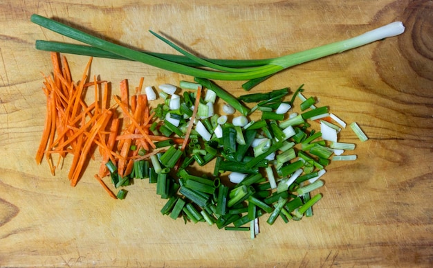 Overhead view of chopped vegetables on a bamboo cutting board\
finely chopped carrots celery onions and garlic on a wooden cutting\
board