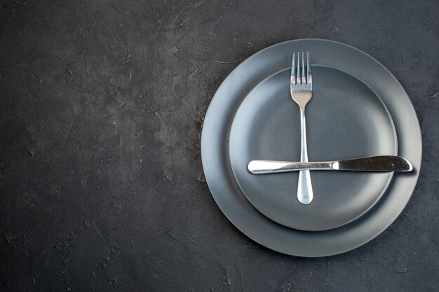 Overhead view of cutlery set on dark color empty plates in two sizes on the left side on black background with free space