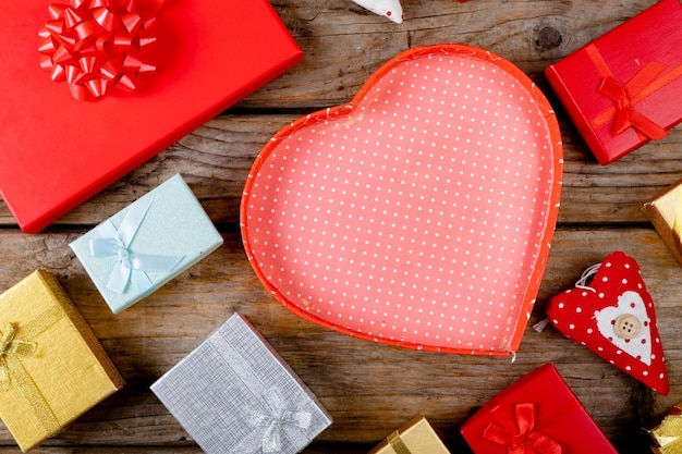 Overhead view of empty red heart shape gift box with copy space amidst presents on wooden table. love and valentine