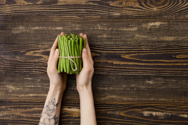 Overhead view of fresh green beans in hand over wooden background