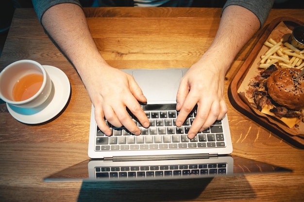 Overhead view hands type on keyboard wooden table burger with mug of tea