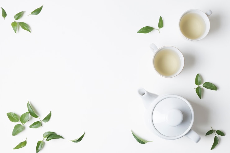  An overhead view of herbal tea cups with leaves and teapot on white background