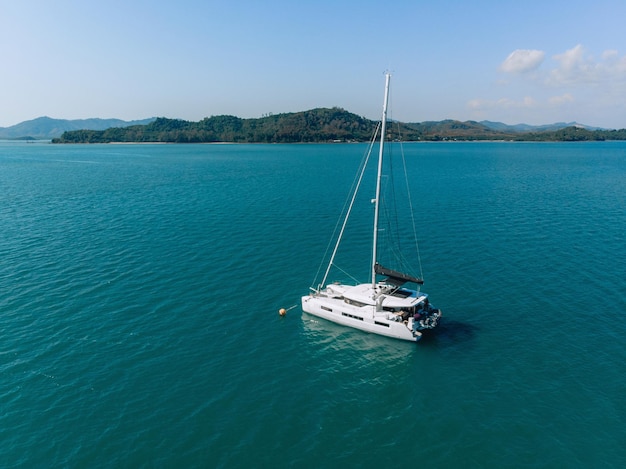 overhead view of a huge laxury boat sailing past, floating alone on the blue water of the sea next to an island filled with forests