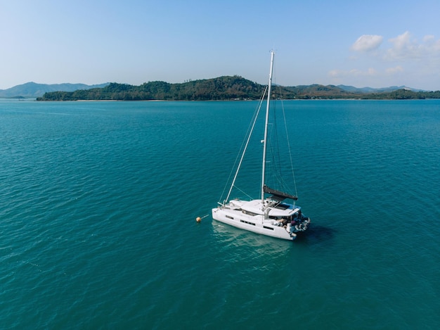 Overhead view of a huge laxury boat sailing past, floating alone on the blue water of the sea next to an island filled with forests