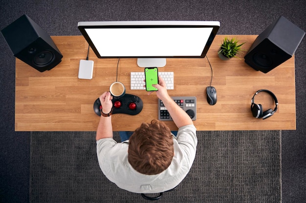 Overhead View Of Male Video Editor Working At Computer In Creative Office Using Mobile Phone