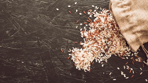 Photo overhead view of mixed rice grains spilling from sack