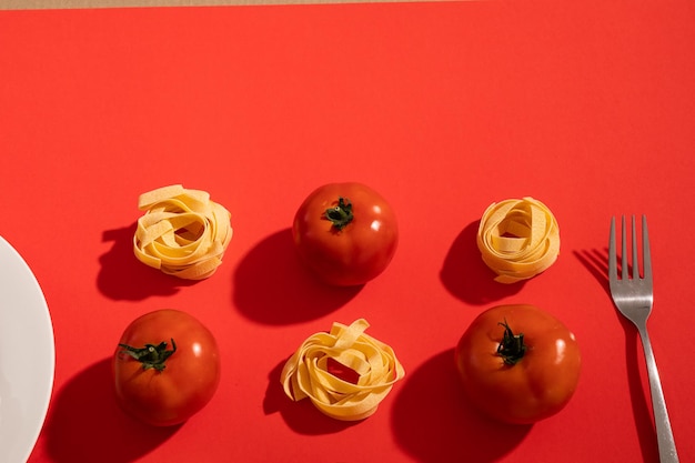 사진 빨간색 배경 위에 복사 공간을 통해 포크와 접시가 있는 토마토와 리본 파스타의 머리 위 전망. 변경되지 않은 유기농 식품과 건강한 식생활 개념.