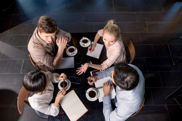 Фото Вид сверху молодых бизнесменов, обсуждающих проект за столом с чашками кофе, бизнес