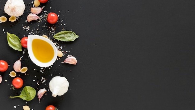 Overhead view of organic cherry tomato; basil leaves; garlic and bowl of olive oil over black surface