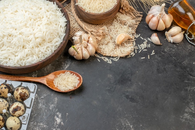 Overhead view of perfect long rice brown bowls on nude color towel fallen oil bottle garlics eggs peppers on dark table