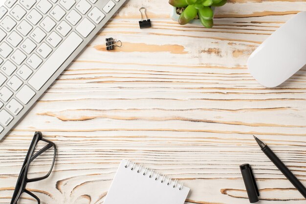 중앙에 빈 공간이 있는 흰색 나무 책상에 있는 바인더 클립 즙이 많은 마우스 펜 나선형 노트북 키보드의 오버헤드 보기 사진