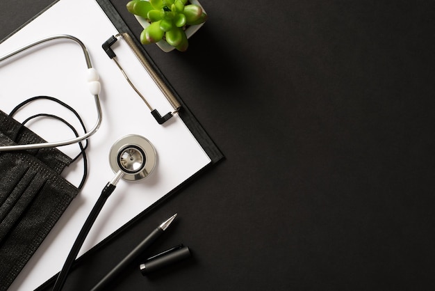 Overhead above view photo of clipboard filter mask flower pot plant stethoscope masks isolated black color backdrop with empty space