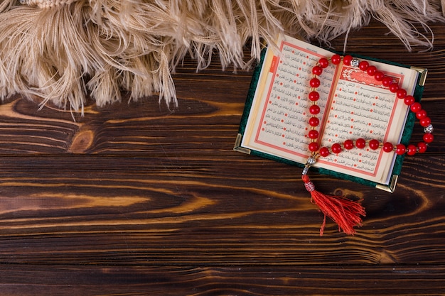 An overhead view of prayer beads with islamic holy book on wooden desk