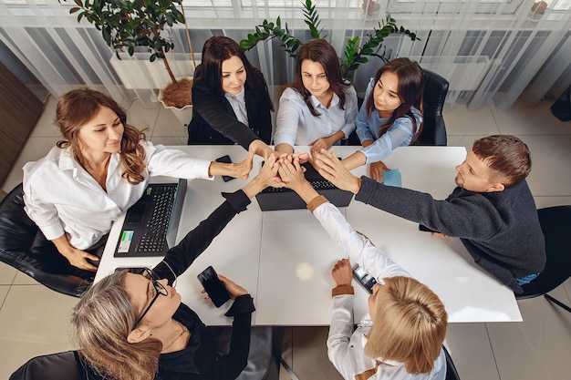 Overhead view of a professional group of business partners rejoicing at work and giving each other a five. A laptop, a telephone and a calculator are on the table. Teamload concept
