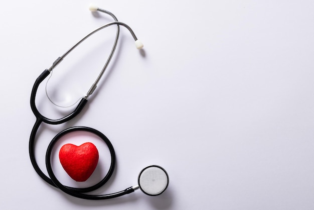 Overhead view of red heart shape with stethoscope against white background, copy space. medical, test, heart, cardiac, disease and healthcare concept.