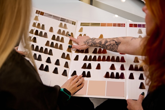 Overhead view to a redhead female hair stylist tattooed hand,on a catalog of hair dye color chart palette and advising customer, hair salon client to choose the color. Professional hair dying concept