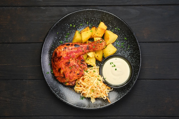 Overhead view of roasted chicken thigh with potato wedges and pickled cabbage