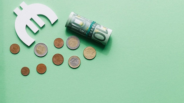 Overhead view of rolled up hundred euro note with symbol and coins on green surface