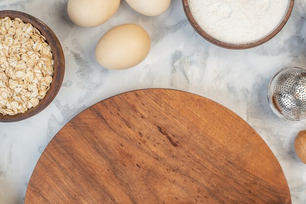 Overhead view of round wooden board among flour eggs walnuts on ice background