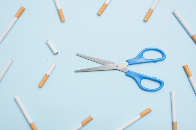 Overhead view of scissor and broken cigarette on blue surface