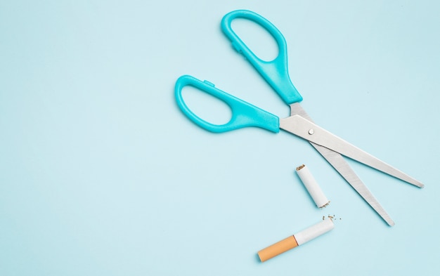 Overhead view of scissor and broken cigarette on colored background