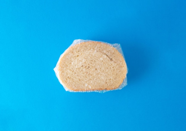 Overhead view of slice of fresh white bread with sesame seeds wrapped in foil against blue background bakery concept