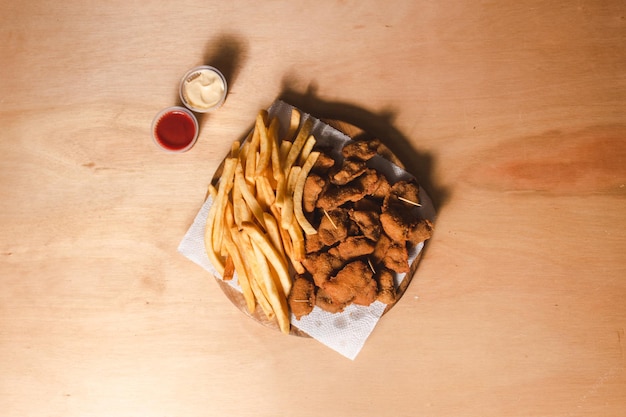 Overhead view of a small snack of bread rolls and french fries with toppings on a wooden table.