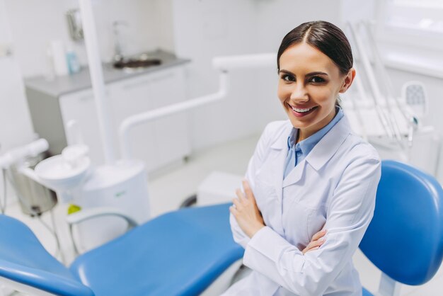 Overhead view of smiling female dentist ith crossed hands looking at the camera in dental clinic