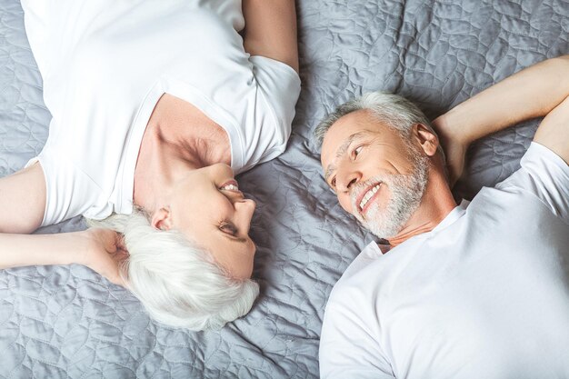 Overhead view of smiling man and woman lying on the bed and looking at each other