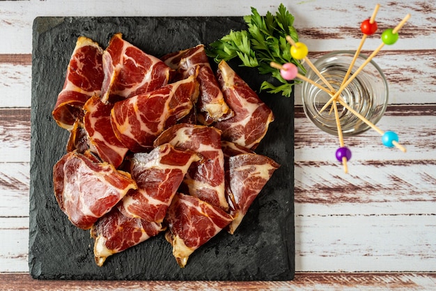 Overhead view of some exquisite fetas de bondiola or raw pickled pork on a black slab.