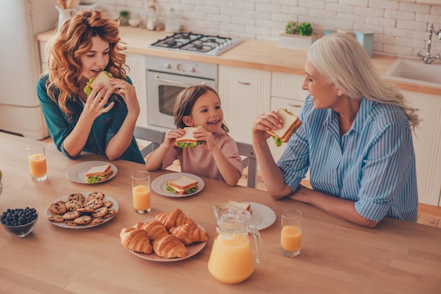 Вид сверху на семью из трех поколений, которая вместе ест бутерброды на завтрак на домашней кухне