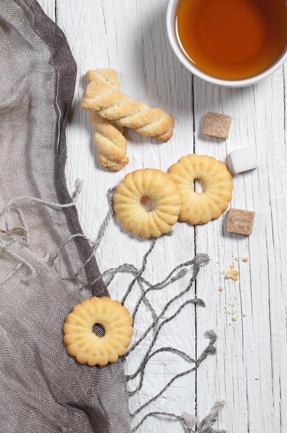 Overhead view of various shortbread cookies and cup of tea on white wooden table