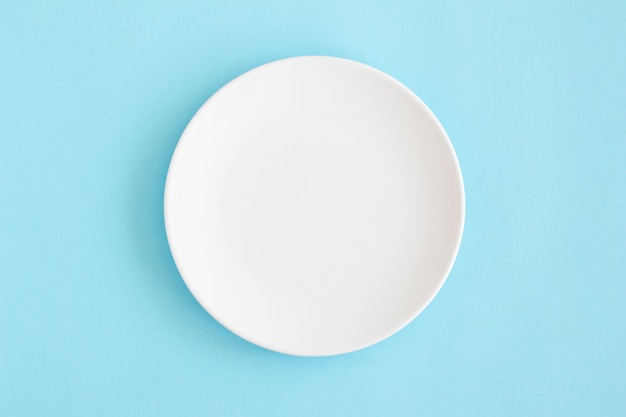 Overhead view of white empty plate on blue background