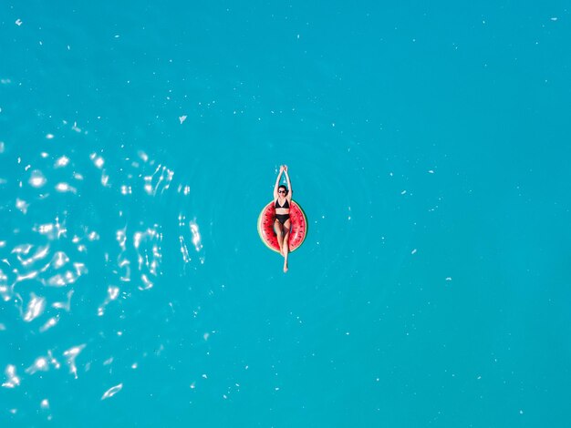 Overhead view of woman floating on inflatable ring in blue sea water