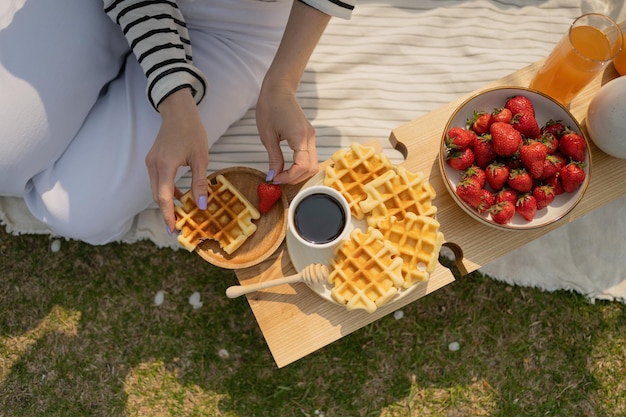 Overhead view of woman having breakfast with waffles and strawberries on wooden tray