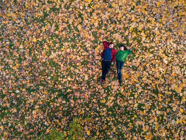 Overhead view of woman with man laying down on the ground covered with autumn leaves