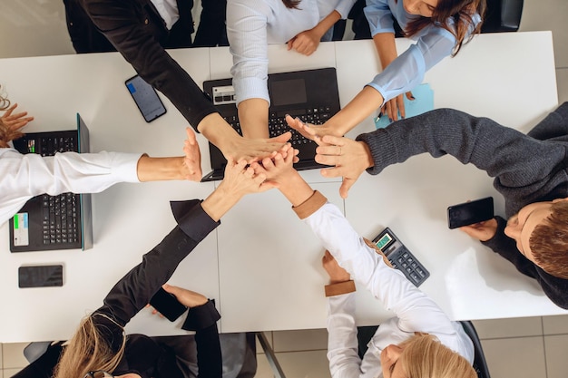 Overhead view of a work successful team and an office white
table on which lying gadgets, laptops and calculators and the hands
of the team are connected in support of teamwork. team concept