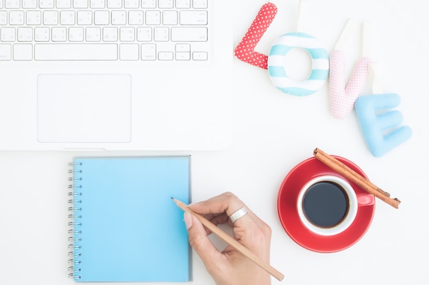 Overhead view of workspace, woman writing on notebook with laptop with love alphabet