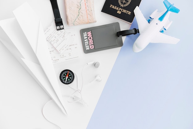 パスポート付き世界旅行者タグのオーバーヘッドビュー。紙飛行機;地図;コンパス;切符売場;おもちゃ飛行機とイヤホンデュアル背景