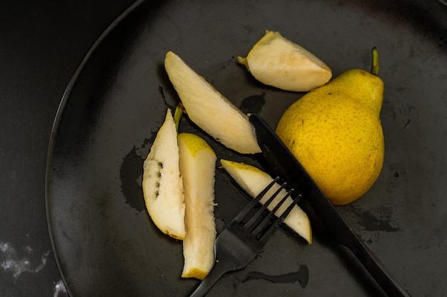 Overhead view of a yellow pear cut into small pieces on a black plate