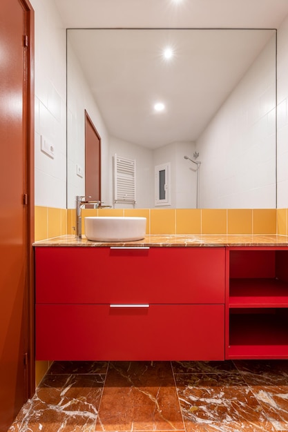 Overhead white sink on a red cabinet in a bright white and yellow bathroom white and yellow tiles on