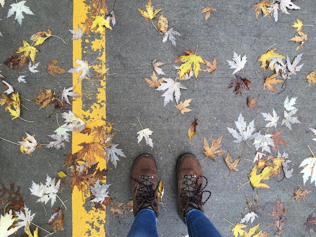 Overhead of woman's legs with boots on ground with fallen leaves, autumn concept