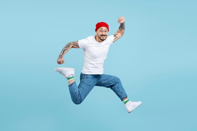 Overjoyed asian man wearing red hat white t shirt stylish shoes jumping high running having fun