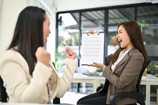 Donne d'affari felicissime che urlano di gioia dopo aver guardato un documento che ottiene una promozione di lavoro