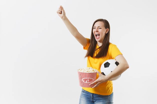 В восторге от европейской молодой женщины, футбольного фаната или игрока в желтой форме, держащего футбольный мяч, ведро попкорна на белом фоне. Спорт, играть в футбол, приветствовать, концепция образа жизни людей болельщиков