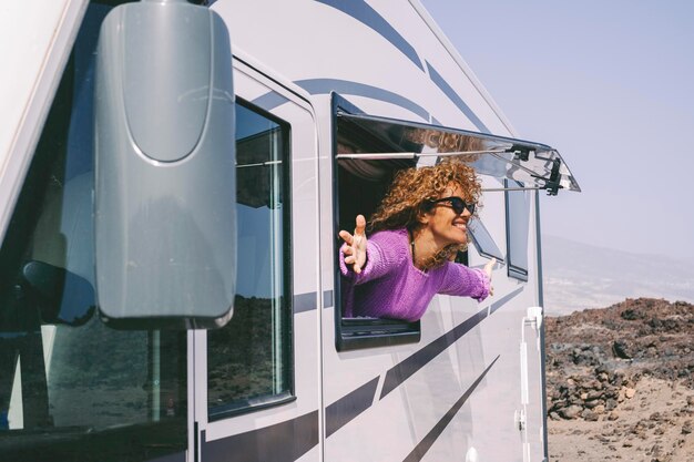 Photo overjoyed and excited adult pretty woman admire outside the camper van window and outstretching arms with big smile concept of tourist people and tourism with rented vehicle nature campsite