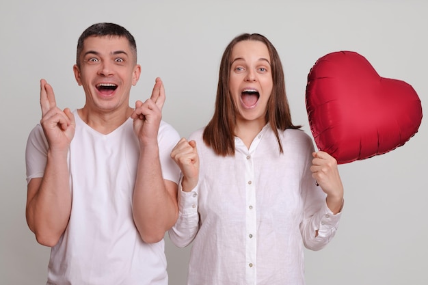 Overjoyed extreem gelukkig positief man en vrouw in witte kleding met een hartvormige luchtballon geïsoleerd over een grijze achtergrond vieren succes en droom uitkomen