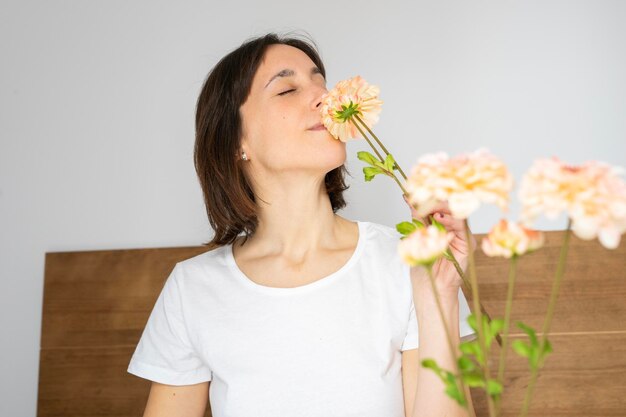 Photo overjoyed girl sitting in bed having breakfast smelling the flowers