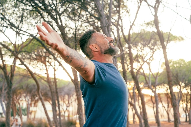 Photo overjoyed happy man enjoying sunset and freedom against a sunset in outdoor leisure activity alone with trees around love for nature planet earth connection mindful and wellbeing travel lifestyle