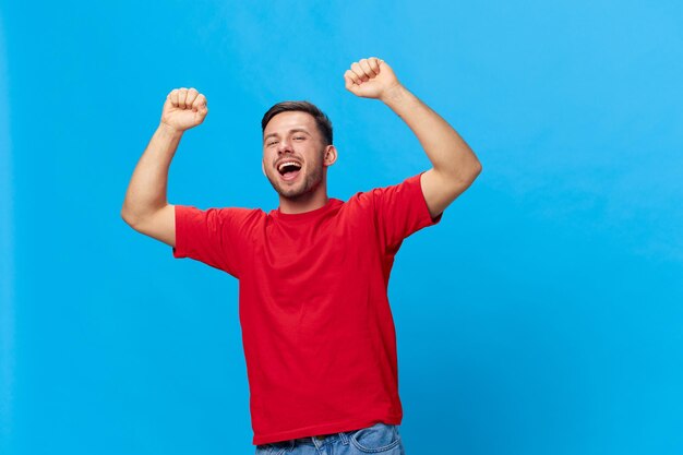 Overjoyed happy tanned handsome man in red tshirt raise fist up\
have big win say yeah posing isolated on blue studio background\
copy space banner mockup people emotions lifestyle concept